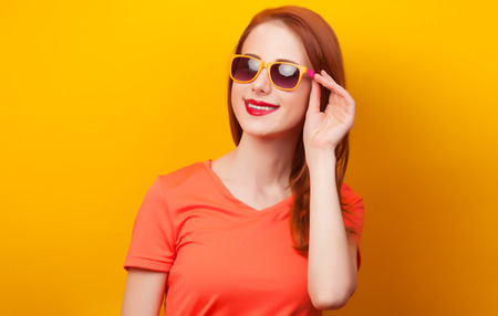 Happy redhead girl in sunglasses on yellow background