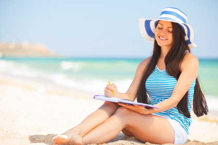 Young brunette girl with note and pencil on the beach in summer time.の写真素材