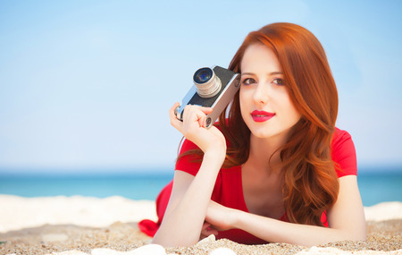 Redhead girl with camera on the beachの写真素材