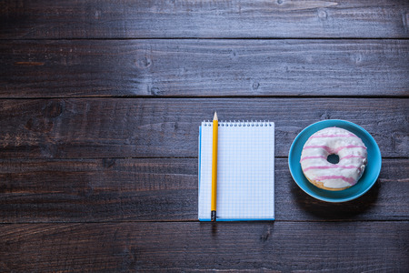 Notebook, donut and pencil on wooden table.の写真素材