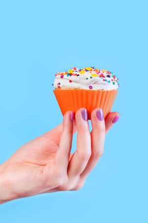 Hand holding cupcake on blue backgroundの写真素材