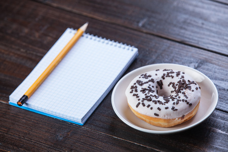 Notebook, donut and pencil on wooden table.の写真素材