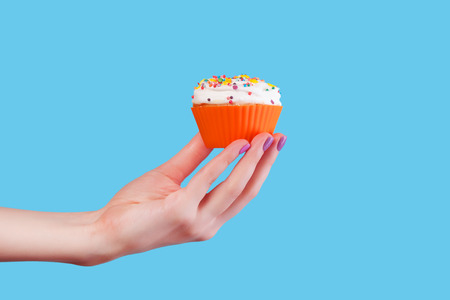 Hand holding cupcake on blue backgroundの写真素材