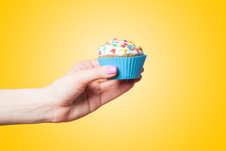 Hand holding cupcake on yellow backgroundの写真素材