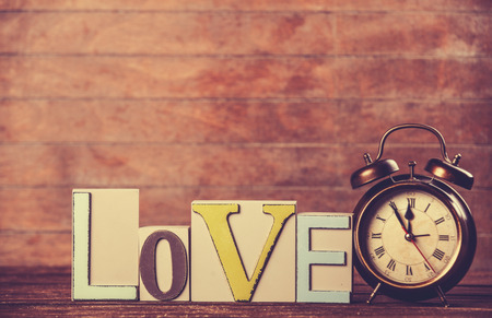 Alarm clock and word Love on wooden table.の写真素材