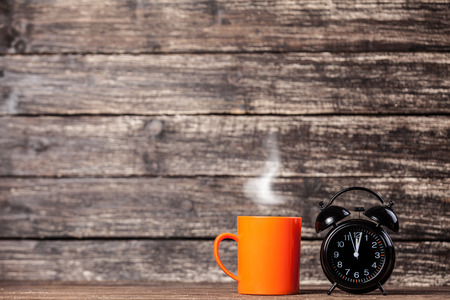 Tea or coffee cup and alarm clock on wooden table.