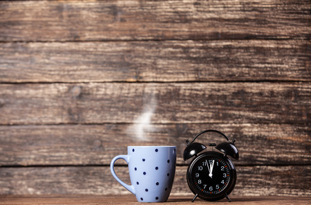 Tea or coffee cup and alarm clock on wooden table.の写真素材