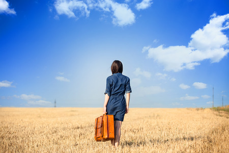 Brunette girl  withsuitcase on wheat field.の写真素材