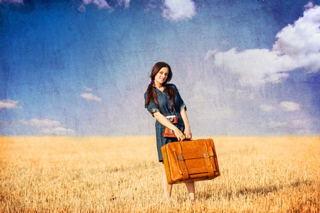 Brunette girl with suitcase on countryside. Photo in old color image style.の写真素材