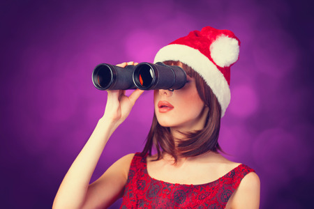 Brunette girl with binocular and hat on violet background.