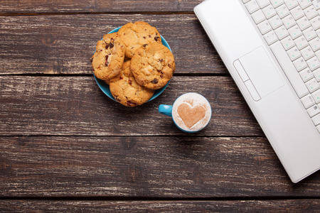 cookie and cup of coffee with laptop on wooden table.の写真素材