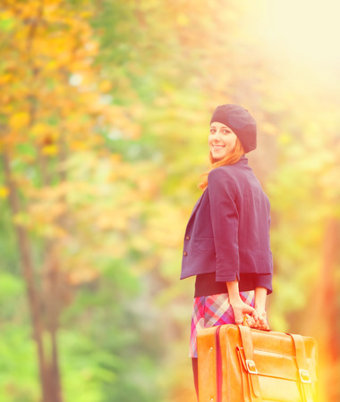 Redhead girl with suitcase at autumn outdoor.の写真素材