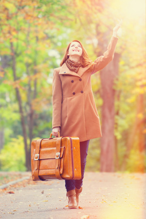 Redhead girl with suitcase at autumn outdoorの写真素材