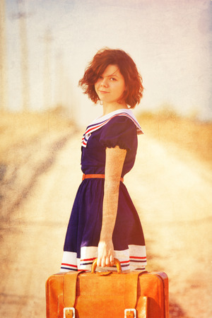 Beautiful brunette girl with suitcase on the countryside road.の写真素材