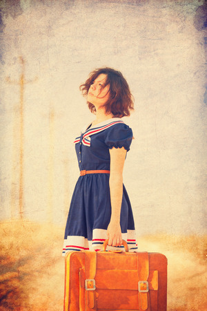 Beautiful brunette girl with suitcase on the countryside road.の写真素材