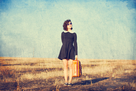 Beautiful brunette girl with suitcase on the fieldの写真素材