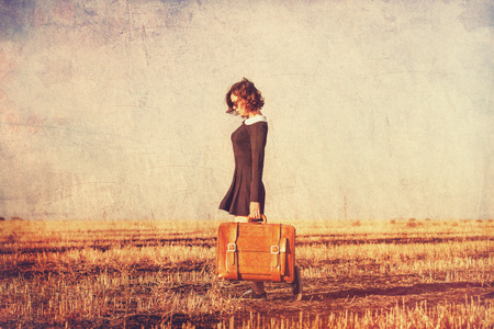 Beautiful brunette girl with suitcase on the fieldの写真素材