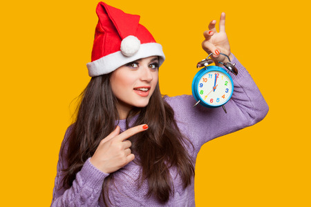 Brunette girl with alarm clock on yellow background.