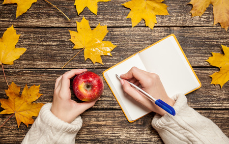 Female hand writing something in to notebook and holding appleの写真素材