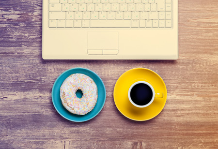Cup of coffee and donut with notebook on a table.の写真素材