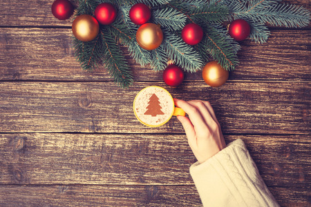 Female holding cup of coffee with cream christmas tree on a table.の写真素材