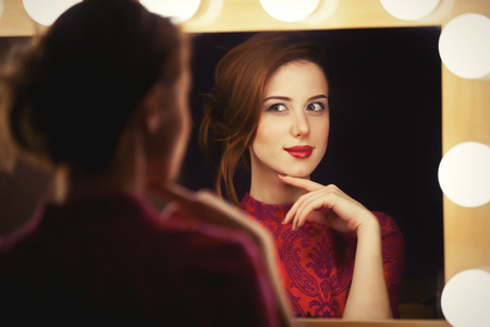 Beautiful redhead women appling makeup near mirrorの写真素材