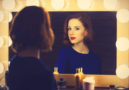 Portrait of a beautiful woman as applying makeup near a mirror. Photo in retro color style.の写真素材