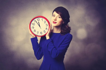 Portrait of beautiful women in blue dress with huge clock on grey background.