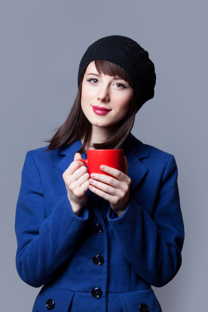 Portrait of beautiful women in blue dress with red cup on grey background.の写真素材