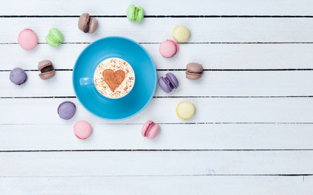 Cup of Cappuccino with heart shape symbol and macaron on white wooden backgroundの写真素材