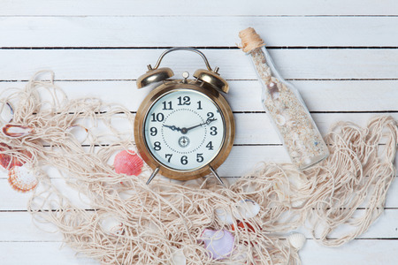 Retro alarm clock and net with shells and bottle on white wooden background.の写真素材