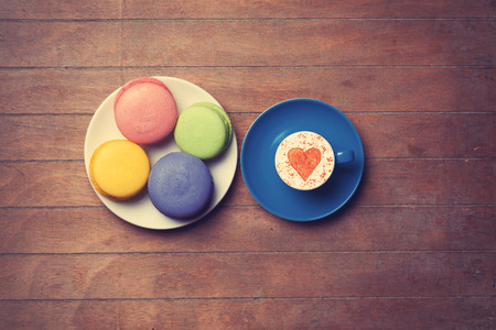 Cup of Cappuccino with heart shape symbol and macarons on wooden backgroundの写真素材