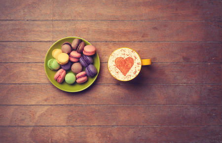 Cup of Cappuccino with heart shape symbol and macarons on wooden backgroundの写真素材