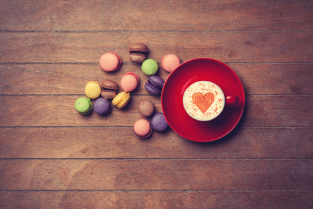 Cup of Cappuccino with heart shape symbol and macarons on wooden backgroundの写真素材