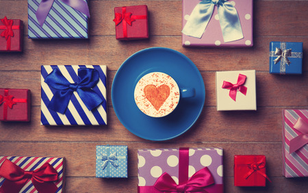 Cup of Cappuccino with heart shape symbol and gift boxes on wooden backgroundの写真素材