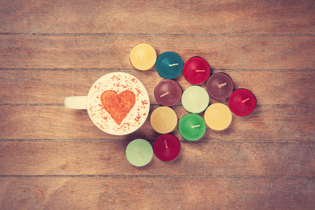 Cup of Cappuccino with heart shape symbol and candles on wooden backgroundの写真素材