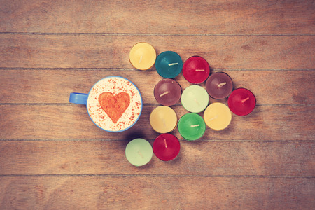 Cup of Cappuccino with heart shape symbol and candles on wooden backgroundの写真素材