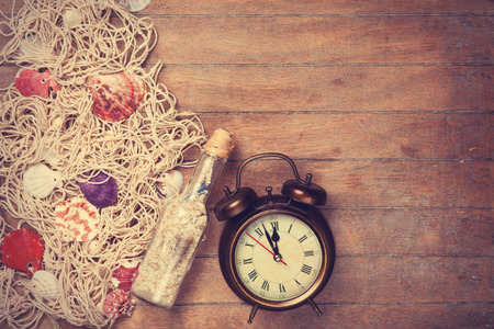 Retro alarm clock and net with shells and bottle on wooden background.の写真素材