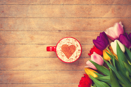 Cappuccino with heart shape near tulips on a table.の写真素材