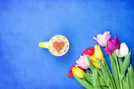 Cup of Cappuccino with heart shape symbol near flowers on blue backgroundの写真素材