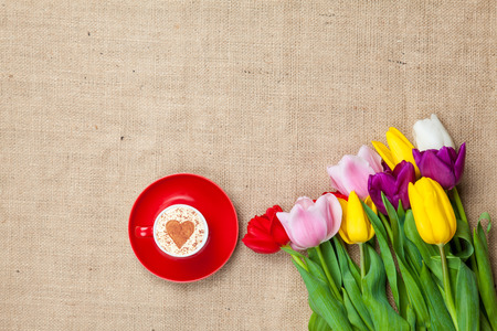 Bouquet of tulips and cup of cuppuccino with heart shape symbol on jute backgroundの写真素材