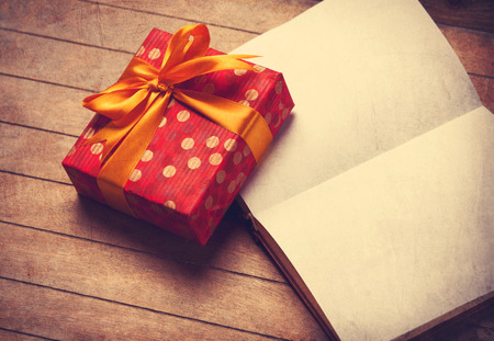 Opened book and gift box on a wooden table. Photo in old color image style.の写真素材