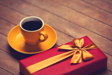 Cup of coffee and gift box on a wooden table. Photo in old color image style.の写真素材