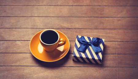 Cup of coffee and gift box on a wooden table. Photo in old color image style.の写真素材