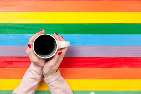 Female hands holding cup of coffee on a color background.の写真素材