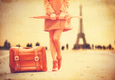 Gril in coat with umbrella and suitcase in Paris on Eiffel tower backgroundの写真素材