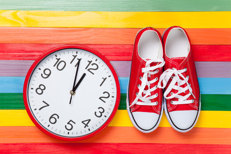 Gumshoes with white shoelaces and clock on multicolor wooden background.の写真素材