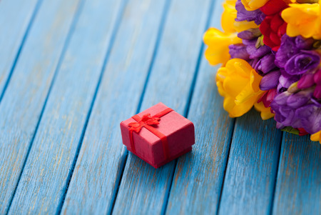Gift box and bouquet of flowers on blue wooden table.の写真素材