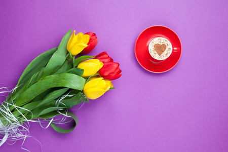 Cup of cappuccino with heart shape and bouquet of tulips on violet background.の写真素材