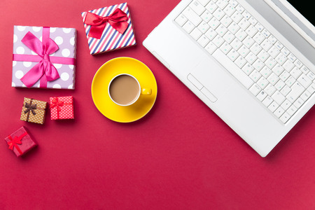 Cup of coffee and gift near computer on red backgroundの写真素材